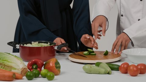 تعلم وتطبيق فنون الطهي، تجهيز مكونات السلطات والاطباق الصحية، المشاركة في تحضير الوصفات الشهية، الاستمتاع بالعمل الجماعي في مهنة الطبخ، تصوير مقرب ليد رجل وامرأة عربيين خليجيين اماراتيان يتشاركان في تجهيز الطعام، امراة خليجيه تقوم بتقطيع الخيارِ