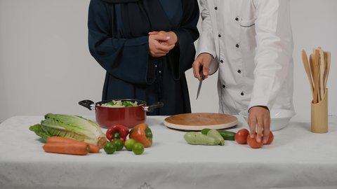 تجهيز مكونات السلطات والاطباق الصحية، تعلم وتطبيق فنون الطهي، المشاركة في تحضير الوصفات الشهية، الاستمتاع بالعمل الجماعي في مهنة الطبخ، تصوير مقرب ليد رجل وامرأة عربيين خليجيين اماراتيان يتشاركان في تجهيز الطعام، رجل خليجي يقوم بتقطيع الطماطم لاعداد السلطة