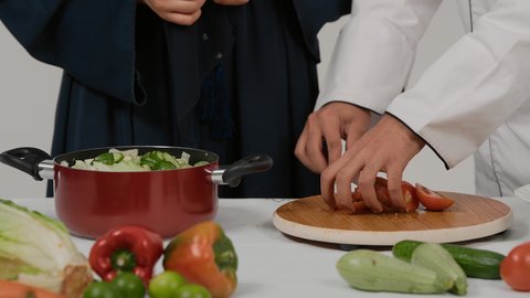 المشاركة في تحضير الوصفات الشهية، الاستمتاع بالعمل الجماعي في مهنة الطبخ، تصوير مقرب ليد رجل وامرأة عربيين خليجيين اماراتيان يتشاركان في تجهيز الطعام، رجل خليجي يقوم بتقطيع الطماطم لاعداد السلطة