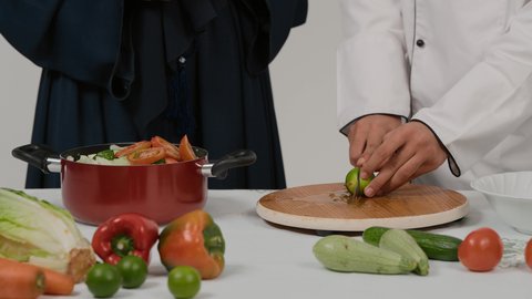 الاستمتاع بالعمل الجماعي في مهنة الطبخ، المشاركة في تحضير الوصفات الشهية، تصوير مقرب ليد رجل وامرأة عربيين خليجيين اماراتيان يتشاركان في تجهيز الطعام، رجل خليجي يقوم يتقطيع اليمون و عصره علي الخضروات