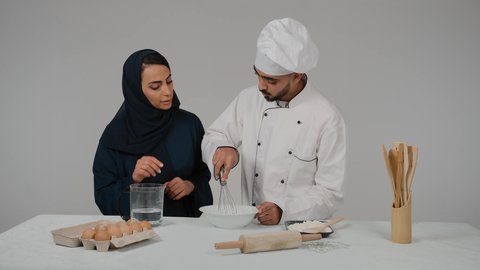 المشاركة في تحضير الوصفات الشهية, الاستمتاع بالعمل الجماعي في مهنة الطبخ، تصوير مقرب لرجل وامرأة عربيين خليجيين اماراتيان يقفان خلف الطاولة الخشبية ويتشاركان في تجهيز الطعام، إعداد السلطات والخضروات والأطباق الصحية، ارتداء زي الشيف والمئزر الأبيض