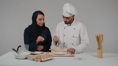 المشاركة في تحضير الوصفات الشهية، الاستمتاع بالعمل الجماعي في مهنة الطبخ، تصوير مقرب لرجل وامرأة عربيين خليجيين اماراتيان يتشاركان في تجهيز الطعام، إعداد المخبوزات والمعجنات الشهية، شيف خليجي يرتدي الزي الخاص بمزاولة المهنة مع القبعه البيضاء يحمل بيده الشوبك