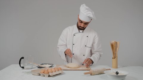 تجهيز المكونات لصناعة الخبز،إعداد المخبوزات والمعجنات الشهية، استخدام أداة فرد العجين، تصوير مقرب لشيف عربي خليجي اماراتي يرتدي الزي الخاص بمزاولة المهنة مع القبعه البيضاء يحمل بيده  الشوبك (النشابة) يقوم بتحضير الطعام، أدوات خاصة بالمطبخ