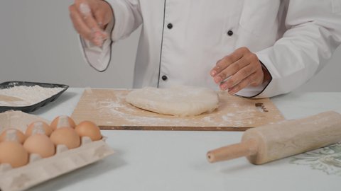 إعداد المخبوزات والمعجنات الشهية، تجهيز المكونات لصناعة الخبز، استخدام أداة فرد العجين، تصوير مقرب ليد شيف عربي خليجي اماراتي يرتدي الزي الخاص بمزاولة المهنة يحمل بيده الشوبك (النشابة) يقوم بتحضير الطعام، أدوات خاصة بالمطبخ