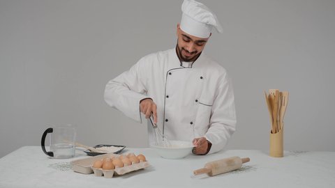 تحضير المخبوزات والفطائر الشهية، مجموعة من المعجنات السهلة والسريعة بأطعمة متنوعة، مخبوزات شعبية طازجة، تصوير مقرب لشيف عربي خليجي اماراتي يرتدي الزي الخاص بمزاولة المهنة مع القبعه البيضاء يحمل بيده الخفاقة اليدوية يقوم بتحضير العجين بايماءات السعاده و السرور