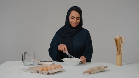 Kitchen tools, expressions of approval and acceptance, preparing delicious baked goods and pastries, the responsibility of the housewife, preparing ingredients for making bread, a close-up of a veiled Emirati Gulf Arab woman wearing a black abaya, holding a hand mixer in her hand, preparing dough with gestures of happiness and pleasure