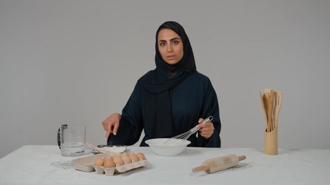إعداد المخبوزات والمعجنات الشهية، أدوات خاصة بالمطبخ، مسؤولية ربة المنزل، تجهيز المكونات لصناعة الخبز، تصوير مقرب لامرأة عربية خليجية اماراتية محجبة ترتدي العباءه السوداء تحمل بيدها الخفاقة اليدوية تقوم بتحضير العجين