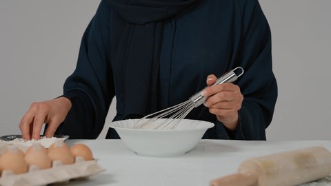 أدوات خاصة بالمطبخ، مسؤولية ربة المنزل، تجهيز المكونات لصناعة الخبز، تصوير مقرب لامرأة عربية خليجية اماراتية محجبة ترتدي العباءه السوداء تحمل بيدها الخفاقة اليدوية تقوم بتحضير العجين، إعداد المخبوزات والمعجنات الشهية