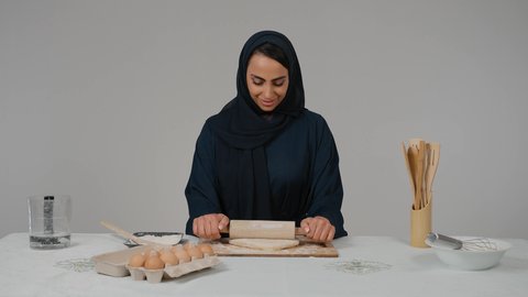 تجهيز المكونات لصناعة الخبز، مسؤولية ربة المنزل، استخدام أداة فرد العجين، تصوير مقرب لامرأة عربية خليجية اماراتية محجبة ترتدي العباءه السوداء تحمل بيدها الشوبك (النشابة) تقوم بتحضير الطعام، أدوات خاصة بالمطبخ، إعداد المخبوزات والمعجنات الشهية