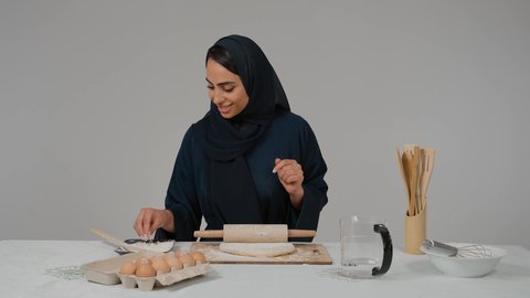 Using a dough rolling tool, a close-up of a veiled Emirati Gulf Arab woman wearing a black abaya holding a rolling pin in her hand, preparing food, preparing ingredients for making bread, kitchen tools, preparing delicious baked goods and pastries, the responsibility of the housewife