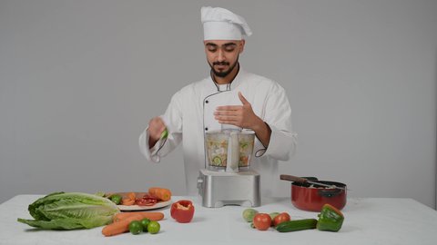 مجموعة من مكونات الخضروات الطازجة على الطاولة لتحضير السلطه، مفهوم النظام الغذائي الصحي، أجهزة كهرومنزلية،تصوير مقرب لشاب عربي خليجي اماراتي يرتدي زي الطهاة الخاص مع القبعه البيضاء يقوم بضرب المكونات في جهاز الخلاط