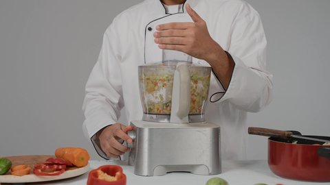Healthy diet concept, home appliances, a set of fresh vegetable ingredients on the table for preparing salad, close-up of a young Emirati Gulf Arab man wearing a special chef's uniform blending ingredients in a blender