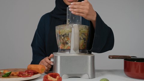 أجهزة كهرومنزلية، مجموعة من مكونات الخضروات الطازجة على الطاولة لتحضير السلطه،تصوير مقرب لامراة عربيه خليجيه اماراتية ترتدي العباءة السوداء تقوم بضرب المكونات بإستخدام جهازالخلاط ، إعداد السلطات الصحية، مفهوم النظام الغذائي الصحي، ، ربة منزل ، التدبير المنزلي