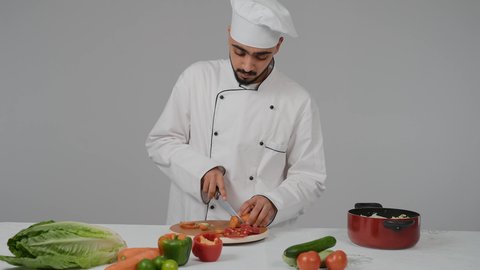 مكونات ووصفات عربية، تقديم المأكولات الشعبية التقليدية الشهية، احتراف مهنة الشيف الطباخ, تصوير مقرب شاب عربي خليجي اماراتي يرتدي زي الطهاة الخاص مع القبعه البيضاء  يقوم بتقطيع الجزرلعمل السلطه الصحيه