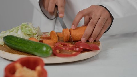 فن الطهي وتقديم الطعام اللذيذ، تقديم المأكولات الشعبية التقليدية الشهية، احتراف مهنة الشيف الطباخ, تصوير مقرب ليد شاب عربي خليجي اماراتي يرتدي زي الطهاة الخاص  يقوم بتقطيع الجزرلعمل السلطه الصحيه