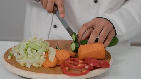 الفن في إعداد وتقديم الأصناف المتنوعة، مهارات تقديم وتزيين الطعام بطرق مميزة ومبتكرة، احتراف مهنة الشيف الطباخ, تصوير مقرب ليد شاب عربي خليجي اماراتي يرتدي زي الطهاة الخاص  يقوم بتقطيع الخيارلعمل السلطه الصحيه