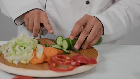 تقديم المأكولات الشعبية التقليدية الشهية، مهارات تقديم وتزيين الطعام بطرق مميزة ومبتكرة، احتراف مهنة الشيف الطباخ, تصوير مقرب ليد شاب عربي خليجي اماراتي يرتدي زي الطهاة الخاص  يقوم بتقطيع الخيارلعمل السلطه الصحيه