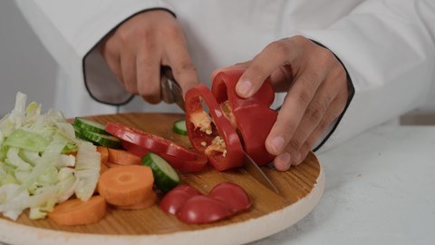 Professional cooking, skills of presenting and decorating food in unique and innovative ways, professional chef cooking, close-up of the hand of a young Emirati Gulf Arab man wearing a special chef's uniform, cutting red peppers to make a healthy salad