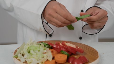 مهارات تقديم وتزيين الطعام بطرق مميزة ومبتكرة، احتراف مهنة الشيف الطباخ, تصوير مقرب ليد شاب عربي خليجي اماراتي يرتدي زي الطهاة الخاص  يقوم بتقطيع الجرير لعمل السلطه الصحي