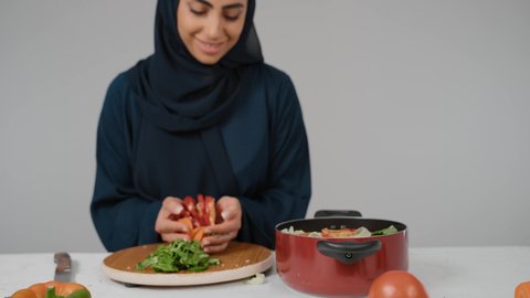 تعلم وتطبيق فنون الطهي ، امراةعربية خليجية اماراتية مبتسمه ترتدي الحجاب والعباءة الكحلي تقوم بتحضير الطعام، طبخ اصناف متنوعه ومختلفه من الماكولات،سيده سعودية تقوم بقضاء أوقات ممتعه  في المطبخ