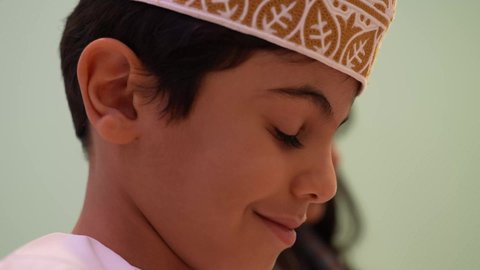 تنميه عقل الاطفال الصغار ، تصوير مقرب لطفل عربي عماني مبتسم يرتدي الدشداشه والكمه ينظر الي الاسفل، أداء الكثير من الأنشطة الممتعة، الاهتمام بالانشطه في رياض الأطفال والحاضنات