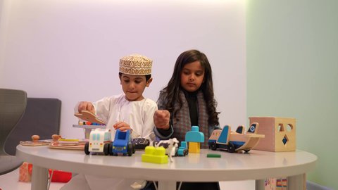 تنمية المهارات والقدرات الذهنية، أطفال عرب عمانيين خليجيين يستمتعون باللعب في المجسمات، أماكن لحضانة الأولاد والاعتناء بهم وتسليتهم، إيماءات السعادة والمتعة، طفل عماني يرتدي الدشداشه والكمه برفقه صديقته في رياض الاطفال