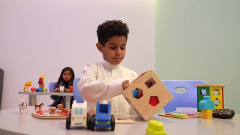 ولد سعودي يقوم بتركيب القطع الملونه بما يناسبها في القطعه الخشبيه، تصوير مقرب ليدين طفل عربي خليجي سعودي في رياض الاطفال، ايماءات يدين تدل علي المشاركه والتشجيع، مهارات تعليميه في رياض الاطفال