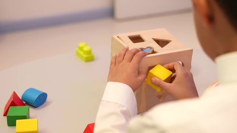 مهارات تعليميه في رياض الاطفال، تصوير مقرب من الخلف ليدين طفل عربي خليجي سعودي في رياض الاطفال، ايماءات يدين تدل علي المشاركه والتشجيع،  ولد سعودي يقوم بتركيب القطع الملونه بما يناسبها في القطعه الخشبيه