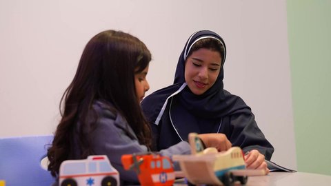 طفله عربيه خليجيه عمانيه تقوم باللعب في السيارات الملونه برفقه معلمتها، معلمة لرياض أطفال عربية سعوديه تختص بالاعتناء بالأطفال، أداء الكثير من الأنشطة الممتعة