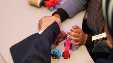 Gestures of participation and encouragement, educational skills in kindergarten, an Omani Gulf Arab teacher playing with the child with colorful car models, a close-up of the hands of a child and a Saudi Gulf Arab teacher in kindergarten
