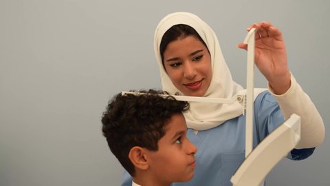 ممرضه عربية خليجية سعوديه تقوم بقياس الطول للطفل، ولد سعودي يرتدي الزي السعودي في موعد مع الطبيبه لعمل الفحوصات اللازمه، مفهوم الطب والرعاية الصحية بالأطفال، الفحص الطبي للأطفال، الرعاية الطبية للأطفال، ادوات طبيه متقدمه للقياس