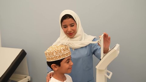 The concept of medicine and healthcare for children, medical examination and medical care, an Omani Gulf Arab female doctor measuring a child's height, an Omani boy wearing a dishdasha and a sleeve in an appointment with the doctor to conduct the necessary tests, advanced medical measuring tools