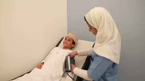 الطب والرعاية الصحية بالأطفال ،الفحص الطبي للأطفال، الرعاية الطبية للأطفال، ادوات طبيه متقدمه ، ممرضه عربية خليجية عمانيه تقوم بقياس الضغط، ولد عماني يرتدي الدشداشه والكمه في،  موعد مع الطبيبه لتلقي العلاج