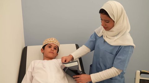 الفحص الطبي للأطفال، الرعاية الطبية للأطفال، ادوات طبيه متقدمه ، ممرضه عربية خليجية عمانيه تقوم بقياس الضغط، ولد عماني يرتدي الدشداشه والكمه في موعد مع الطبيبه لتلقي العلاج، مفهوم الطب والرعاية الصحية بالأطفال