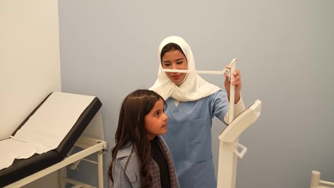 ممرضه عربية خليجية سعوديه تقوم بقياس الطول للطفله، بنت سعوديه ترتدي الزي الكاجوال في موعد مع الطبيبه لعمل الفحوصات اللازمه، مفهوم الطب والرعاية الصحية بالأطفال، الفحص الطبي للأطفال، الرعاية الطبية للأطفال، ادوات طبيه متقدمه للقياس