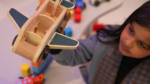 الجلسات والحصص الإبداعية في الروضات السعودية، طفله عمانيه ترتدي الجاكيت تستمتع باللعب بايماءات وجه مبتسم، مهارات وأنشطة تساعد على التطور الفكري، ، تصوير مقرب لطفله سعوديه تقوم باللعب بمجسم الطائره بايماءه التركيز