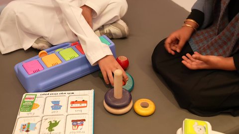 A Saudi girl in a kindergarten and nursery is putting the colored rings in their place with the help of her friend, a close-up of an Arab Gulf Omani child using the stacking rings game with his friend, an Arab Omani kindergarten that specializes in taking care of children, performing many fun activities