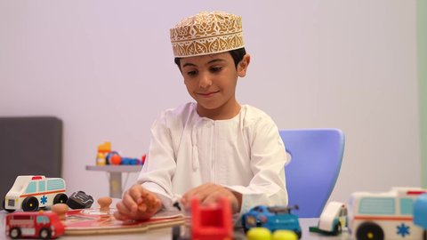 تصوير مقرب لطفل عربي خليجي عماني يرتدي الدشداشه والكمه يقوم بمحاوله تركيب القطع في مكانها الصحيح، رياض أطفال عربية عمانيه تختص بالاعتناء بالأطفال، أداء الكثير من الأنشطة الممتعة، طفل عماني في رياض الأطفال والحاضنات