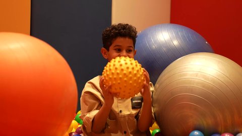 الالعاب الاكترونية الترفيهيه ، التسلية و الترفيه في الخارج، طفل سعودي في مدينة الألعاب بتعابير وجه تدل على السعادة ، قضاء اوقات رائعة في مدينة الملاهي ،ولد عماني يرتدي الزي الكاجوال يستمتع باللعب في حوض مليئ بالكور الملونه اثناء العطلة الصيفية