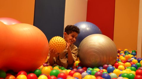 طفل سعودي في مدينة الألعاب بتعابير وجه تدل على السعادة ، قضاء اوقات رائعة في مدينة الملاهي ، العاب الكترونية الترفيهيه ، التسلية و الترفيه في الخارج، ولد عماني يرتدي الزي الكاجوال يستمتع باللعب في حوض مليئ بالكور الملونه اثناء العطلة الصيفية