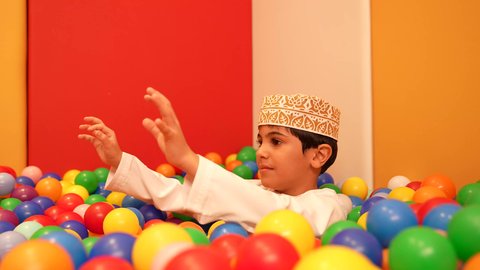 الاهتمام بالاطفال في الروضة،  حضانة أطفال في سلطنه عمان،مشاركه اللعب بين الاطفال، ولد عماني يرتدي الدشداشه والكمه يقوم باللعب في حوض الكور البلاستيكية الملونه، ايماءه الفرح والسرور