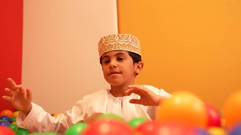 حضانة أطفال في سلطنه عمان، الاهتمام بالاطفال في الروضة، مشاركه اللعب بين الاطفال، ولد عماني يرتدي الدشداشه والكمه يقوم باللعب في حوض الكور البلاستيكية الملونه، ايماءه الفرح والسرور