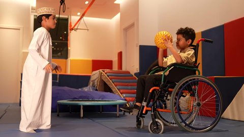 طفلان عربيان خليجيان عمانيان مبتسمان يقومان باللعب سويا في المدرسه، ولد عماني يرتدي الدشداشه والكمه يقوم باللعب بالكره برفقه صديقه، تعليم وابداع و تنمية المهارات، الاهتمام بالاطفال في الروضة، الرعايه الخاصه بذوي الاحتياجات الخاصه