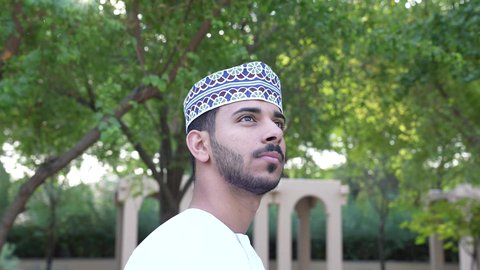 الاستجمام بالطبيعة واستنشاق الهواء الطلق، الخروج إلى أحد الاماكن العامة للترفيه عن النفس،  رجل عربي خليجي عماني يرتدي الزي العماني يسير فى احدي حدائق سلطنة عمان ، الاستمتاع بالأجواء في إحدى المنتزهات