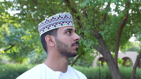 الخروج إلى أحد الاماكن العامة للترفيه عن النفس،  رجل عربي خليجي عماني يرتدي الزي العماني يسير فى احدي حدائق سلطنة عمان ،  الاستجمام بالطبيعة واستنشاق الهواء الطلق،الاستمتاع بالأجواء في إحدى المنتزهات