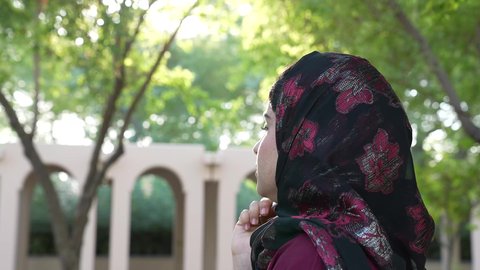 تصوير من الخلف لامراه عربيه خليجية عمانية ترتدي العباءه والحجاب تقوم بتدخين الفيب ، القيام بعادات سلوكية ضارة،سيدة سعودية تتعاطي النيكوتين عبر السيجاره الالكترونيه في الهواء الطلق