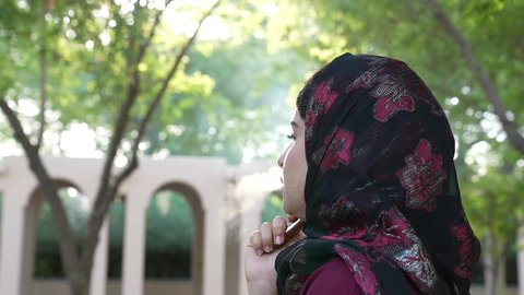 القيام بعادات سلوكية ضارة، تصوير من الخلف لامراه عربيه خليجية عمانية ترتدي العباءه والحجاب تقوم بتدخين الفيب ، سيدة سعودية تتعاطي النيكوتين عبر السيجاره الالكترونيه في الهواء الطلق