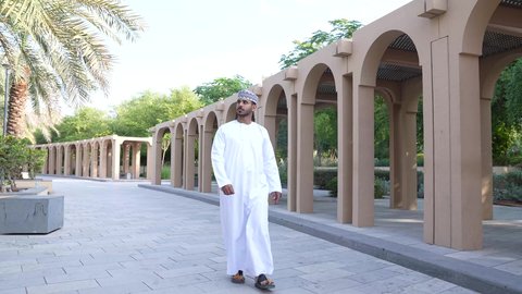 الاستجمام بالطبيعة واستنشاق الهواء الطلق، الخروج إلى أحد الاماكن العامة للترفيه عن النفس، الاستمتاع بالأجواء في إحدى المنتزهات، رجل عربي خليجي عماني يرتدي الزي العماني يسير فى احدي حدائق سلطنة عمان