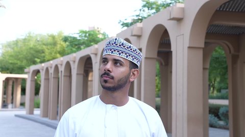 رجل عربي خليجي عماني يرتدي الزي العماني يسير فى احدي حدائق سلطنة عمان ،الخروج إلى أحد الاماكن العامة للترفيه عن النفس، الاستجمام بالطبيعة واستنشاق الهواء الطلق، الاستمتاع بالأجواء في إحدى المنتزهات