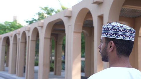 رجل عربي خليجي عماني يرتدي الزي العماني يسير فى احدي حدائق سلطنة عمان ،الخروج إلى أحد الاماكن العامة للترفيه عن النفس، الاستجمام بالطبيعة واستنشاق الهواء الطلق، الاستمتاع بالأجواء في إحدى المنتزهات